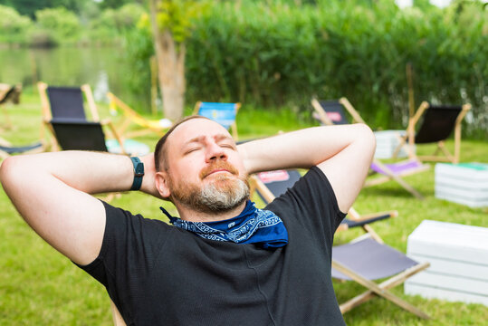 adult man relaxes outdoor in a city beach garden holding hands behind head. solo outdoor activities