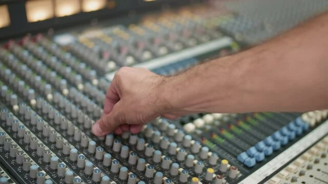 Close up of unrecognizable male hand turning channels on mixing console for adjusting sound at control room of recording studio