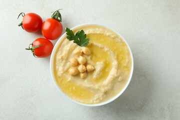 Bowl of hummus and tomatoes on white textured background