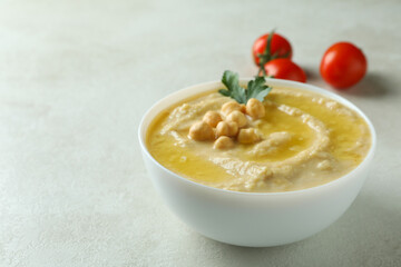Bowl of hummus and tomatoes on white textured background