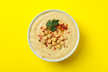 Bowl of fresh hummus on yellow background