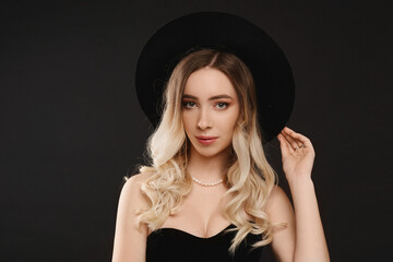 Portrait of a sexy model woman with perfect slim body in a black bodysuit and black stylish hat over black background