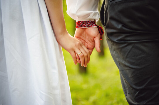 Look at the hands of two lovers who are holding each other. Close-up. Wrist. cropped image. Girl in white dress and man in shirt. Walk around the park.