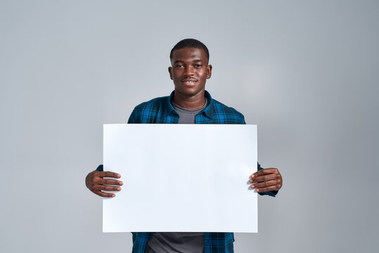 Cheerful young african american man in casual clothes smiling at camera, displaying blank banner ad, holding it in front of him, posing isolated over gray background