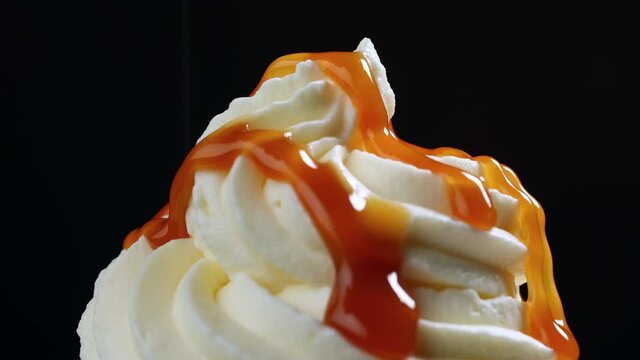 melted caramel sauce flowing on rotating whipped cream close up on black background