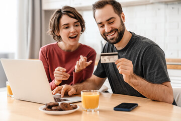 Fototapeta na wymiar Happy young couple using laptop and credit card while sitting at home