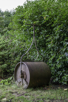 Vertical Shot Of An Old And Rustic Cricket Pitch Roller With Green Leaves In The Background