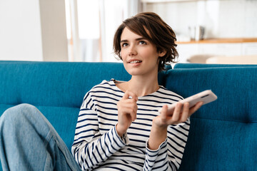 Thinking beautiful woman using mobile phone while sitting on couch