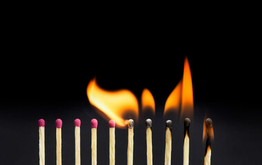 Close-up of burning matches igniting other matchsticks in a row against a black background. Chain reaction concept.