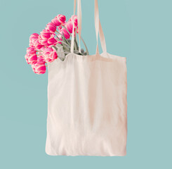 Pink tulips bunch in white cotton shopping bag with copy space at light blue wall background....