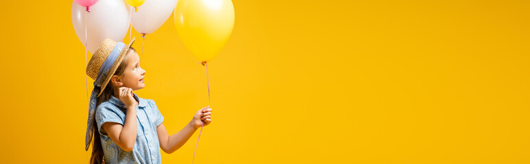 happy kid in straw hat looking at balloons isolated on yellow, banner © LIGHTFIELD STUDIOS