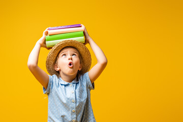 surprised kid in straw hat holding books above head isolated on yellow