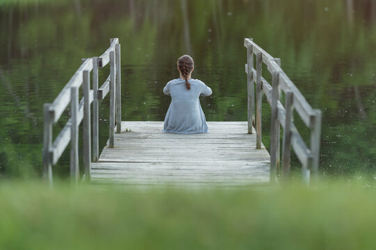 mujer sentada de espaldas en embarcadero en el lago