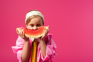 Girl in raincoat covering face while looking at watermelon isolated on crimson