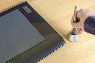 A man's hand retrieves a pen for a graphic tablet from a special stand.