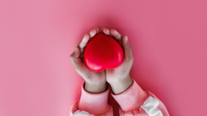 Little girl holding red heart in hand on pink background