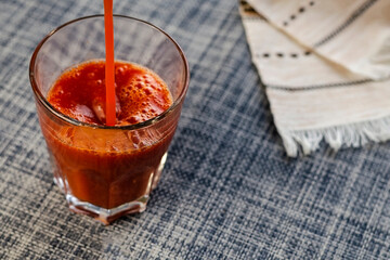 A thin stream of tomato juice fills the glass.