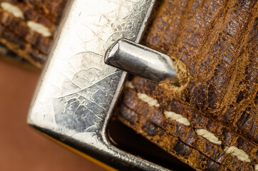 A closeup of an old metal buckle of a brown leather trouser belt.