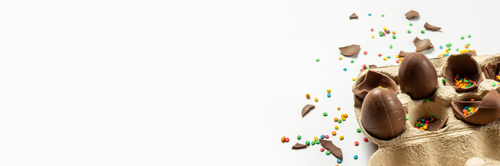 Tray with broken Easter chocolate eggs and multi-colored sweet candy decorations on a light background. Easter concept, easter treats, bunny. Banner