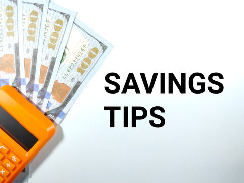 Selective focus.Text SAVINGS TIPS on a white background with calculator and fake dollar money.Savings concept idea.Shot were noise and film grain.