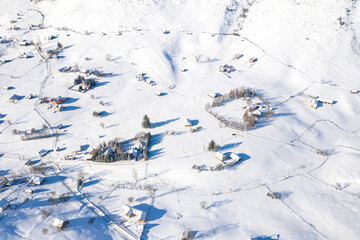 Fototapeta na wymiar Aerial scenic rural view of Sirnea village at the bottom of Piatra-Craiului Mountains in freezing winter landscape from Romania