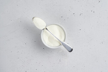 Collagen powder in a silver spoon and white ceramic bowl on concrete background.