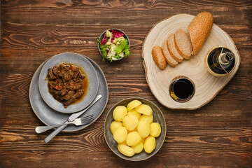 Overhead view of beef ragout with potato, salad and wine