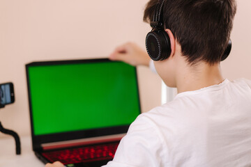 Young boy in headphones open laptop and start playing games. Handsome teenage boy steamer