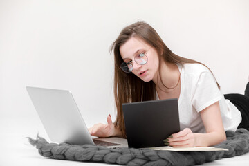 Naklejka premium A seriously young girl in glasses sits with a laptop. Education, remote work and blogging. Isolated on a white background.