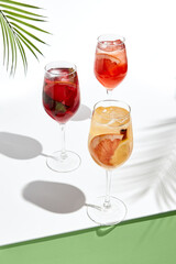Assortment of sangria drinks on white table. Sunshine with hard shadow. Palm leaves and shadow. Fresh, summer, tropic, beach drink concept