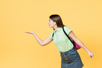 Smiling teen girl with backpack pointing with hand isolated on yellow