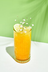 Mango lemonade drink over green background. White table with sunlight and palm leaf hard shadow. Summer, tropical and juicy concept