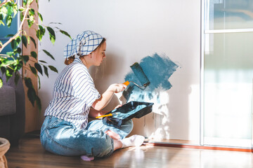 young girl paints the wall of the house with a roller in blue. Gender equality, stereotypes, March 8. Hobby, work as a house painter. Comfort, spring renewal, home decor.Selective focus