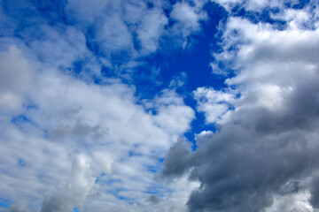 White clouds in the blue sky. Natural summer background. Thickening of rain clouds in one place.