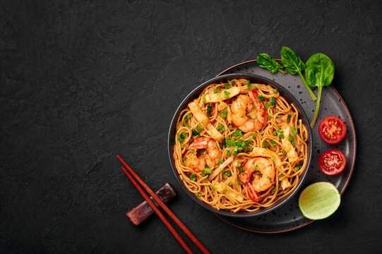 Mie Goreng in black bowl on dark slate table top. Indonesian cuisine prawn noodles and vegetables stir fired dish. Asian food. Top view. Copy space