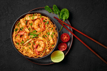 Mie Goreng in black bowl on dark slate table top. Indonesian cuisine prawn noodles and vegetables stir fired dish. Asian food. Top view