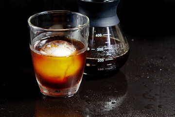 Cold americano decoration with ice ball in whisky glass on a black table.