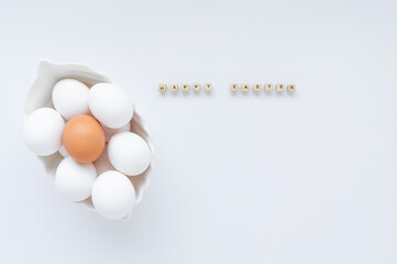 Many white eggs and one brown egg in a white dish and the inscription Happy Easter on a light...