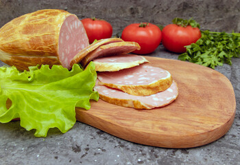 Traditional large sliced ​​sausage on a cutting board. Green salad and tomatoes. Homemade food. View from above. Close-up.