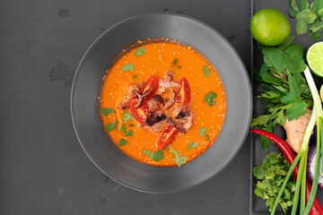 Tom yam Thai soup in black bowl served on gray background