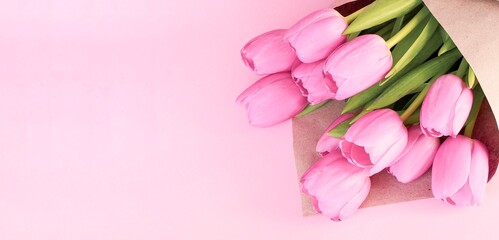 Bouquet of tulips wrapped in craft paper on pink background with space for text. Greeting card. Concept woman's or mother's day. Spring flowers background. Banner