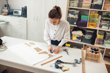 a young girl seamstress applies a sketch with a piece of soap on the fabric from which she will sew clothes