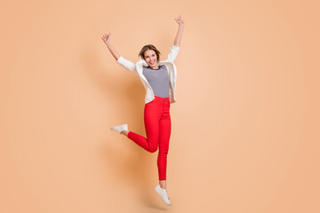 Fototapeta na wymiar Full size photo of young happy excited smiling cheerful girl jumping in victory isolated on beige color background