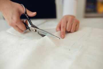 Close-up female hands cuts out a piece of fabric on which a chalk pattern of clothing is marked for tailors