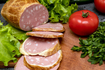 Traditional large sliced ​​sausage on a cutting board. Green salad and tomatoes. Homemade food. View from above. Close-up.
