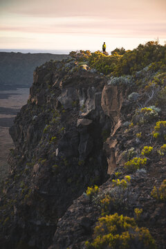 Man standing on a rocky cliff at sunset near a volcano