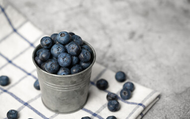 Fresh blueberries in a small metal bucket surrounded with some berries on a checked napkin. Top view. Rustic.