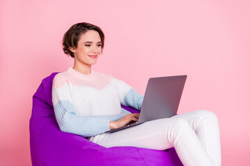 Photo portrait of woman browsing internet on laptop sitting in violet beanbag chair isolated on pastel pink colored background