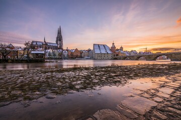 Naklejka premium Sonnenuntergang während Hochwasser des Flusses Donau im Winter 2021 in Regensburg mit Blick auf den Dom die Altstadt und überschwemmte Promenade und der steinerne Brücke, Deutschland