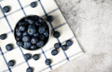 Fresh blueberries in a small metal bucket surrounded with some berries on a checked napkin. Top view. Rustic.